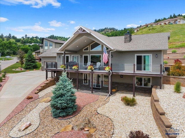 rear view of property with a wooden deck, a patio area, a chimney, and a shingled roof