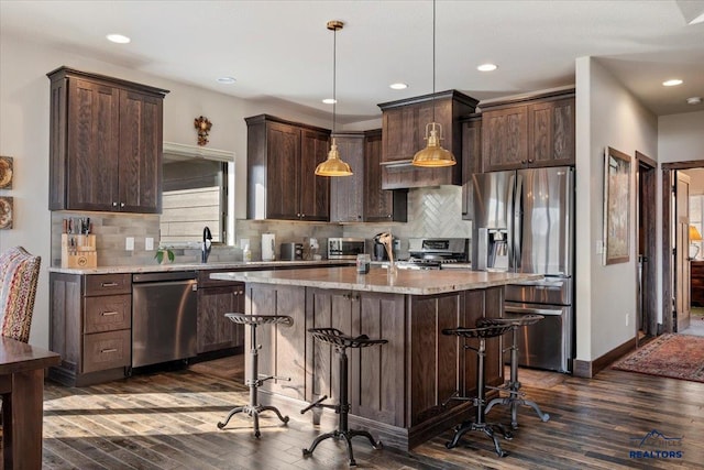 kitchen featuring a center island, dark brown cabinetry, a kitchen bar, stainless steel appliances, and dark wood-style flooring