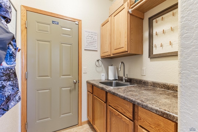 kitchen with a textured wall, a sink, and dark countertops