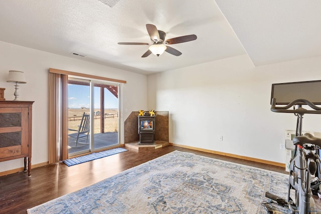 living area with a ceiling fan, wood finished floors, a wood stove, baseboards, and visible vents