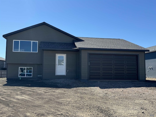 split level home featuring an attached garage, a shingled roof, and dirt driveway