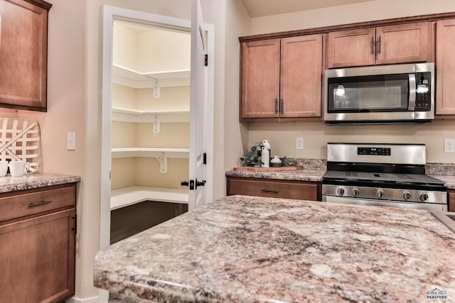 kitchen featuring light stone countertops, brown cabinetry, and appliances with stainless steel finishes