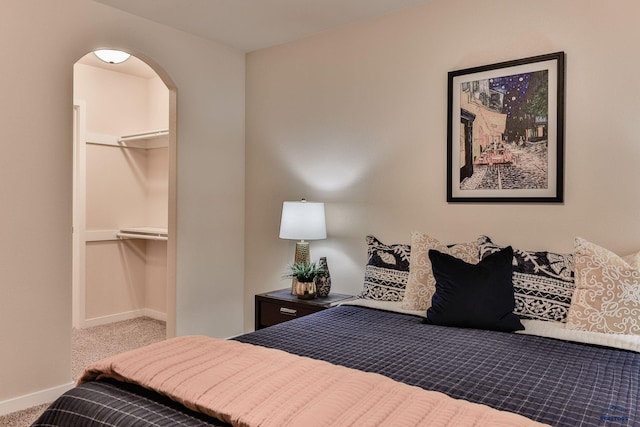 bedroom with a closet, baseboards, arched walkways, a spacious closet, and carpet