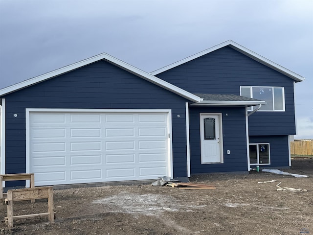 split level home featuring a garage, fence, and dirt driveway