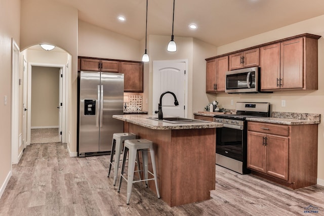 kitchen with a kitchen breakfast bar, light wood-style flooring, a kitchen island with sink, stainless steel appliances, and a sink