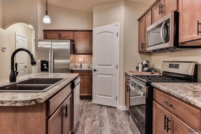 kitchen with hanging light fixtures, a sink, an island with sink, wood finished floors, and stainless steel appliances