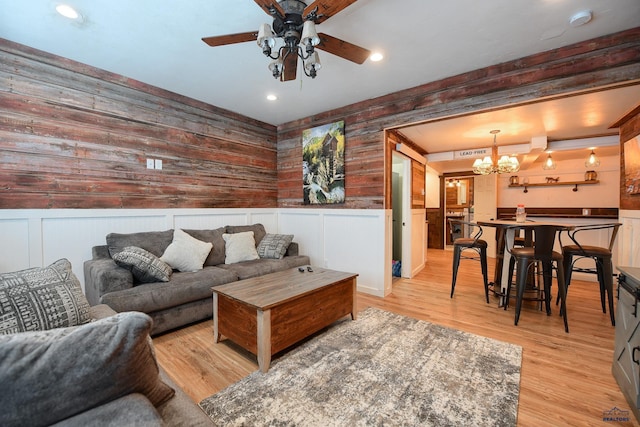 living area with a wainscoted wall, ceiling fan with notable chandelier, and light wood-style floors