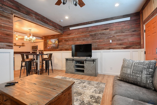 living area featuring recessed lighting, ceiling fan with notable chandelier, a wainscoted wall, beam ceiling, and wood finished floors