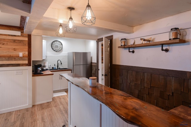 kitchen featuring wooden counters, a sink, a wainscoted wall, beam ceiling, and freestanding refrigerator