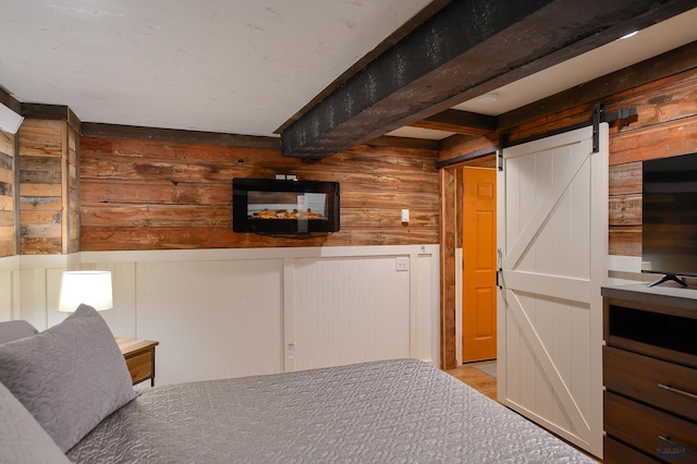 interior space with a barn door, wood finished floors, beam ceiling, and wood walls