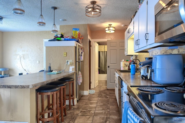 kitchen featuring stainless steel microwave, a sink, a textured ceiling, range with electric cooktop, and a textured wall