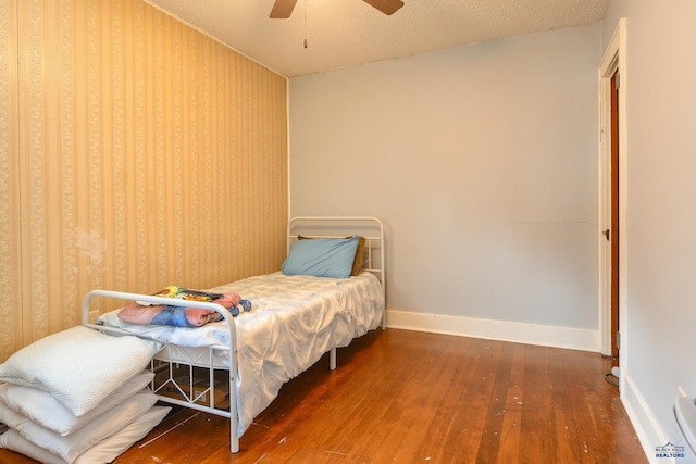 bedroom featuring baseboards, wallpapered walls, hardwood / wood-style flooring, and a ceiling fan