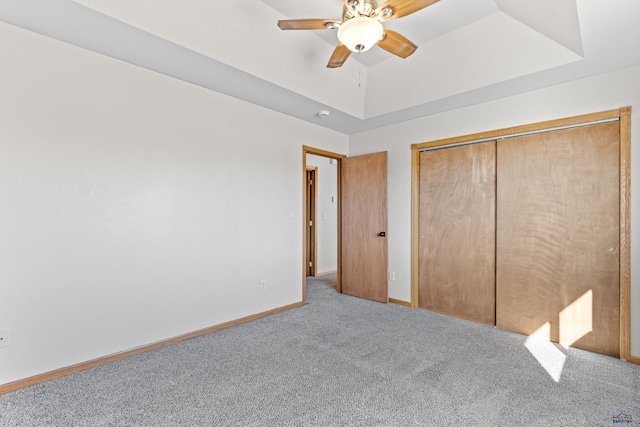 unfurnished bedroom featuring a tray ceiling, carpet, baseboards, ceiling fan, and a closet