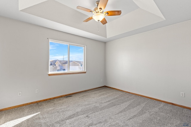 carpeted empty room featuring baseboards, a tray ceiling, visible vents, and ceiling fan
