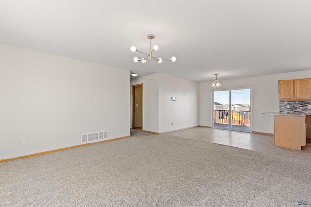 unfurnished living room with light colored carpet, visible vents, baseboards, and a chandelier
