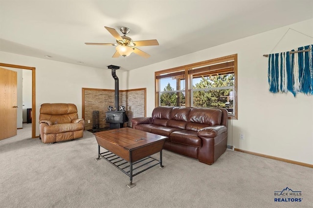 living area featuring baseboards, a wood stove, a ceiling fan, and light carpet