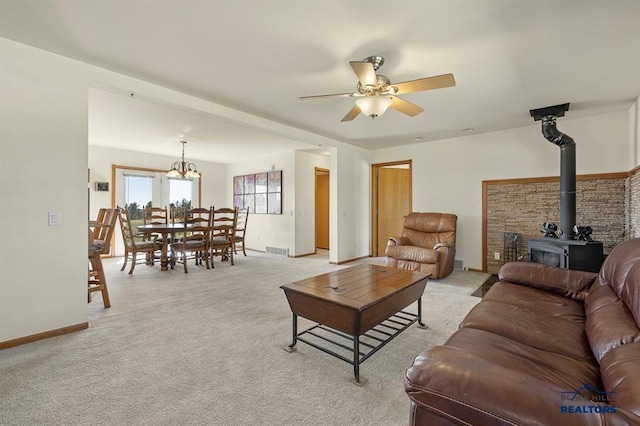 living area with light colored carpet, a wood stove, ceiling fan with notable chandelier, baseboards, and visible vents