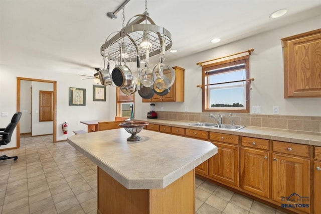 kitchen with light countertops, a sink, a kitchen island, brown cabinetry, and recessed lighting