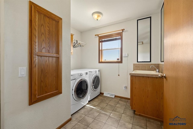washroom featuring a sink, washing machine and clothes dryer, laundry area, baseboards, and visible vents