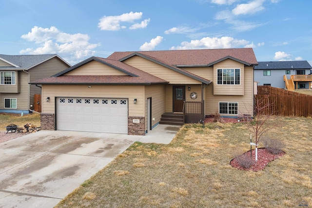 split level home featuring concrete driveway, an attached garage, fence, brick siding, and a shingled roof