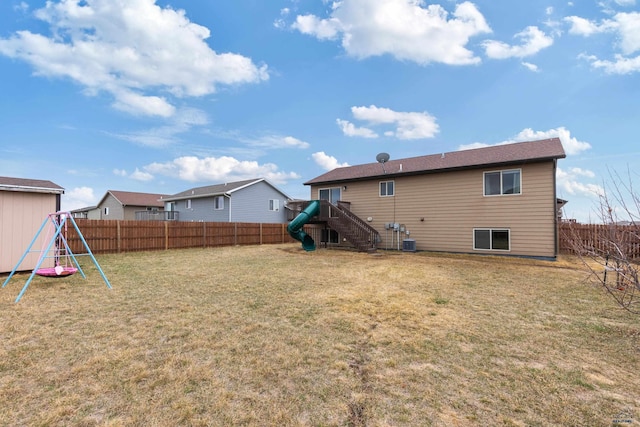rear view of property with a yard, central AC unit, a fenced backyard, and a playground