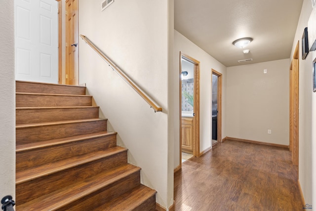 foyer featuring baseboards, visible vents, wood finished floors, and stairway