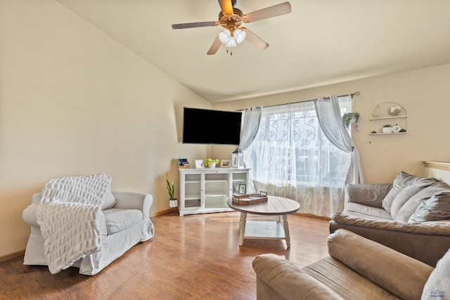 living area with baseboards, lofted ceiling, wood finished floors, and a ceiling fan