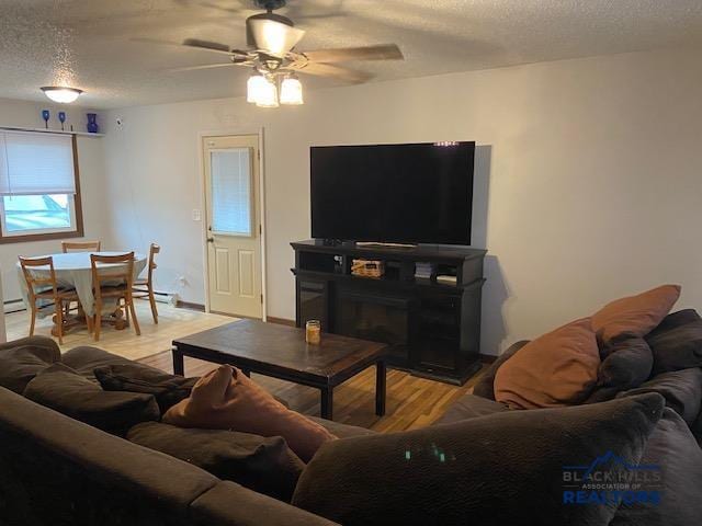 living area featuring baseboard heating, a textured ceiling, a ceiling fan, and light wood finished floors