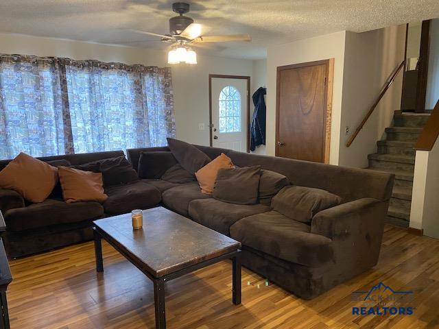 living room featuring wood finished floors, ceiling fan, stairway, and a textured ceiling