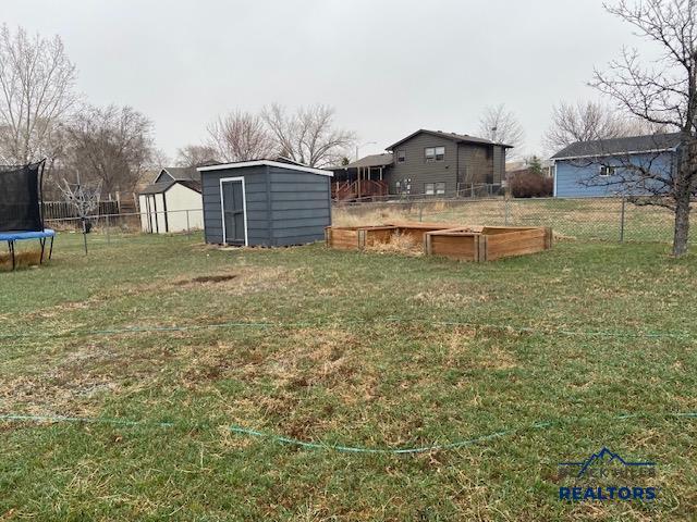 view of yard featuring a trampoline, an outdoor structure, a storage shed, a fenced backyard, and a vegetable garden