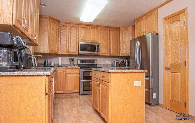 kitchen featuring appliances with stainless steel finishes, light wood-style floors, a center island, and light stone counters