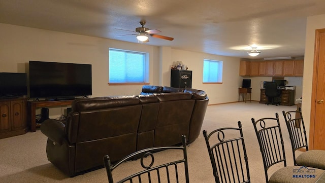 living room featuring light colored carpet, a desk, a ceiling fan, and baseboards