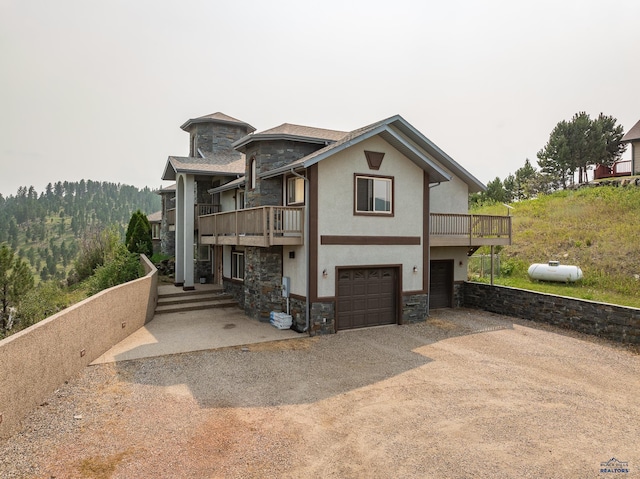 23863 Emerald Pines Dr, Hill City, SD 57745 - view of front of home with stucco siding, stone siding, a balcony, driveway, and a garage