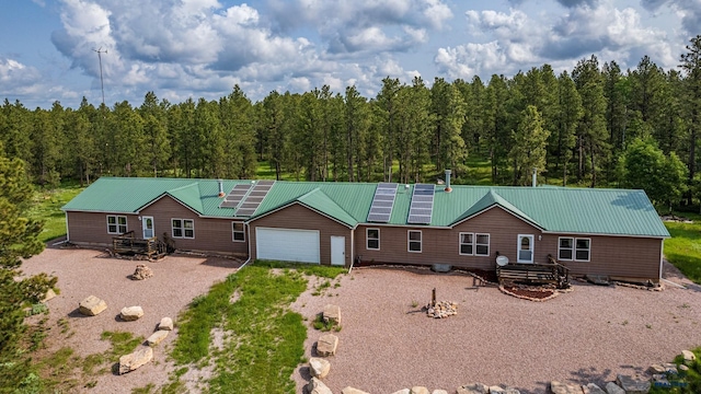 view of front of house with driveway, metal roof, solar panels, a detached garage, and a wooded view