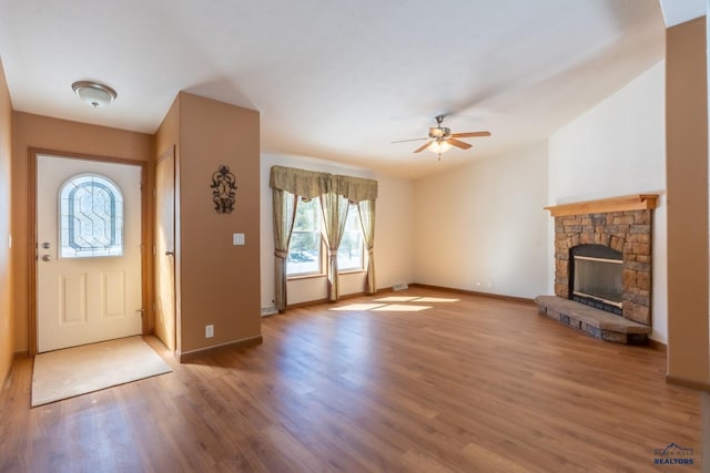 entryway featuring a stone fireplace, baseboards, wood finished floors, and a ceiling fan