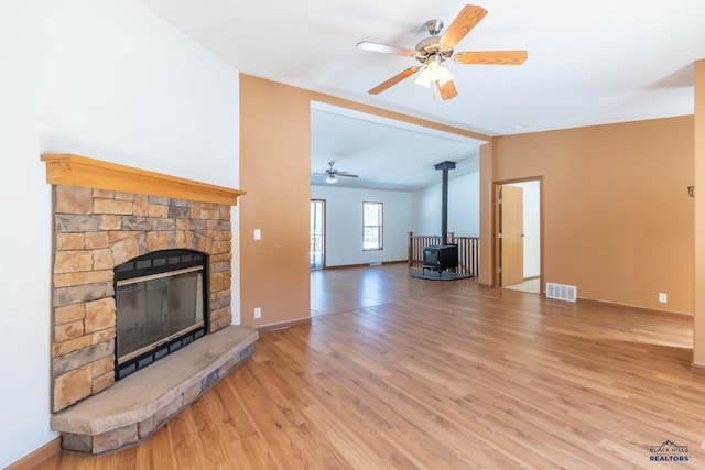 unfurnished living room featuring vaulted ceiling, a wood stove, light wood finished floors, ceiling fan, and visible vents