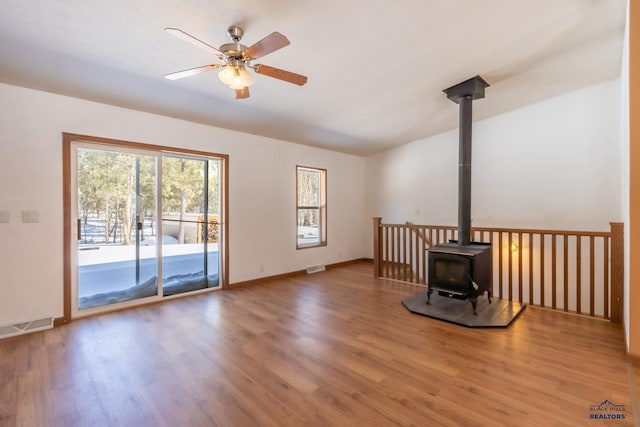 unfurnished living room featuring a ceiling fan, visible vents, wood finished floors, and a wood stove