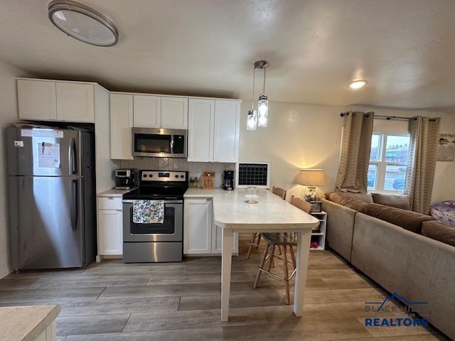 kitchen with backsplash, a peninsula, open floor plan, light wood-type flooring, and stainless steel appliances