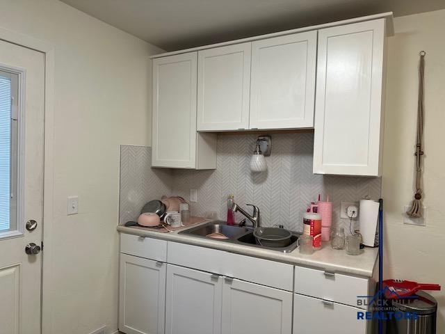 kitchen featuring backsplash, white cabinets, a sink, and light countertops