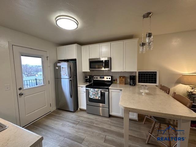 kitchen with light countertops, stainless steel appliances, light wood finished floors, white cabinets, and a peninsula