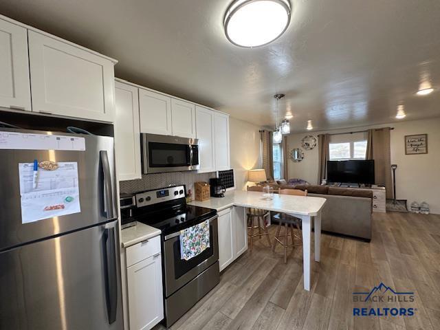 kitchen with open floor plan, light wood-style flooring, appliances with stainless steel finishes, and a peninsula