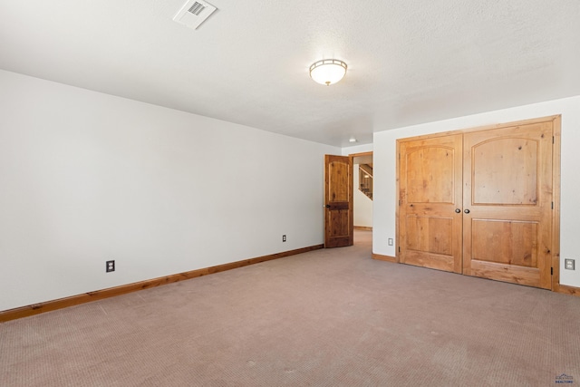 unfurnished bedroom with a closet, a textured ceiling, baseboards, light colored carpet, and visible vents