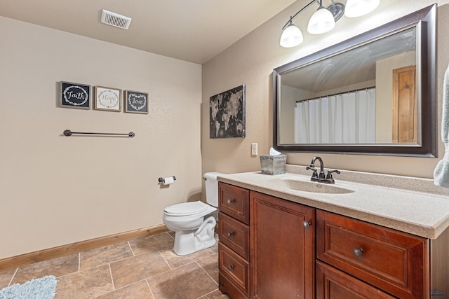 bathroom featuring vanity, toilet, stone finish floor, baseboards, and visible vents