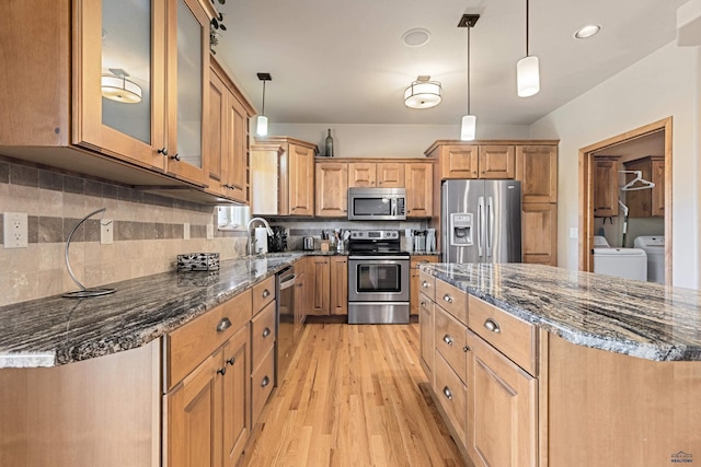kitchen featuring washer and clothes dryer, stainless steel appliances, dark stone countertops, backsplash, and a sink