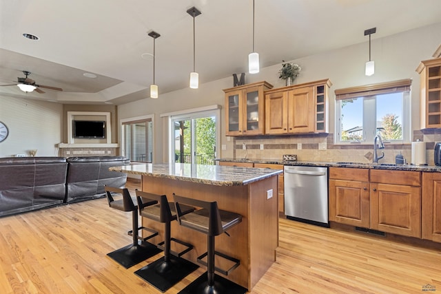 kitchen featuring a kitchen island, a sink, stone counters, light wood finished floors, and dishwasher
