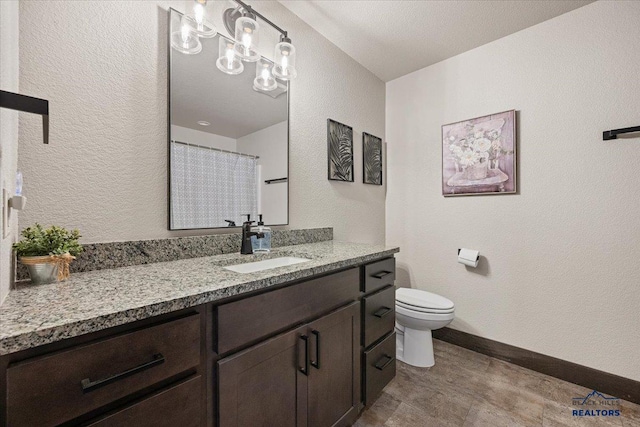 full bath featuring toilet, curtained shower, vanity, baseboards, and a textured wall