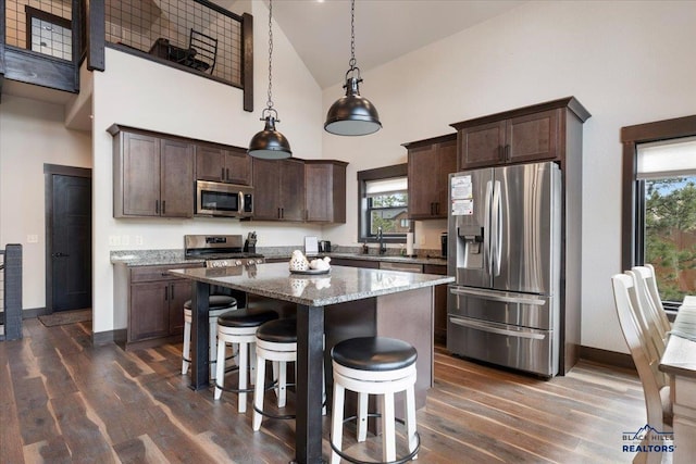 kitchen with stainless steel appliances, dark wood finished floors, a sink, light stone countertops, and dark brown cabinets
