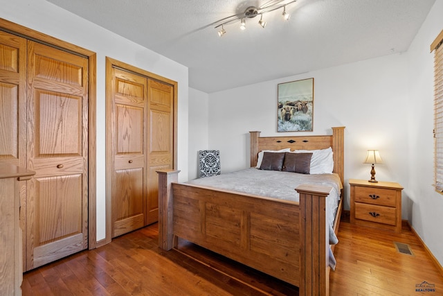 24354 Rushmore Ranch Rd, Keystone, SD 57751 - bedroom featuring a textured ceiling, visible vents, two closets, and wood-type flooring