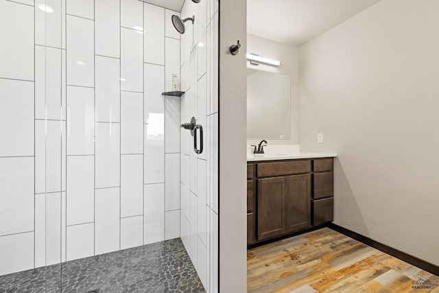 bathroom featuring vanity, baseboards, a tile shower, and wood finished floors