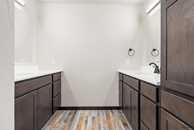 bathroom with baseboards, a sink, two vanities, and wood finished floors